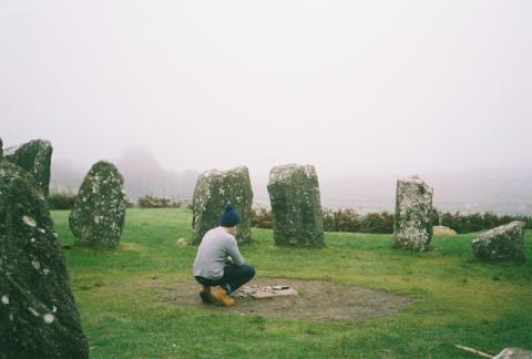 A stone circle, with somebody crouching at its center