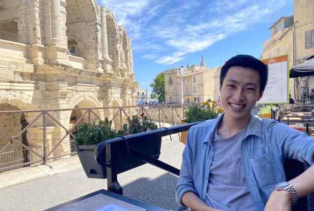 a student smiles for a photo while at an outdoor cafe by Les Arenas in Arles