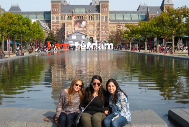 three students sitting in front of the I Amsterdam sign