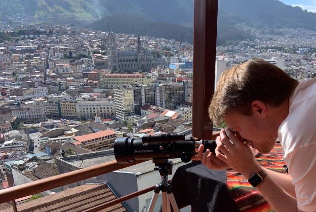 a student looks through a telescope from the top of a building in Quito's city center