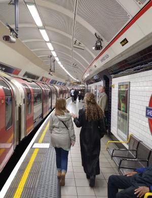 two students walking along the platform shepard's bush in london whle a train passes on the left