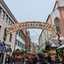 Sign arching over a street that says "Wehnachtsmarkt," wooden stalls lining the street. 