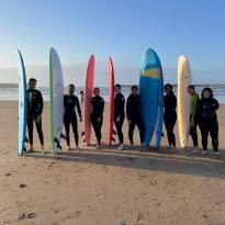 A group of students with surf boards standing in front of the ocean