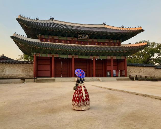 a student poses for a photo at Changdeokgung Palace in Seoul in a traditional Korean hanbok dress and umbrella