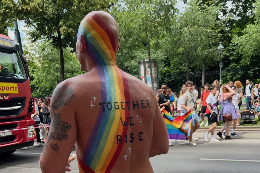 This is an image of a person attending the Pride Parade, with a rainbow painted across his back and the words "together we rise".