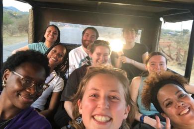 group of students sitting in a safari car smiling with sunset coming through back window