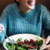 In a booth, a woman in a blue sweater is eating a salad.