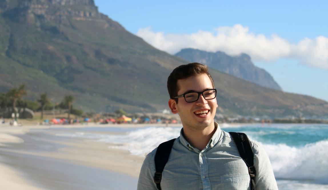 a male student smiling on the beach in Cape Town with moutains behind him