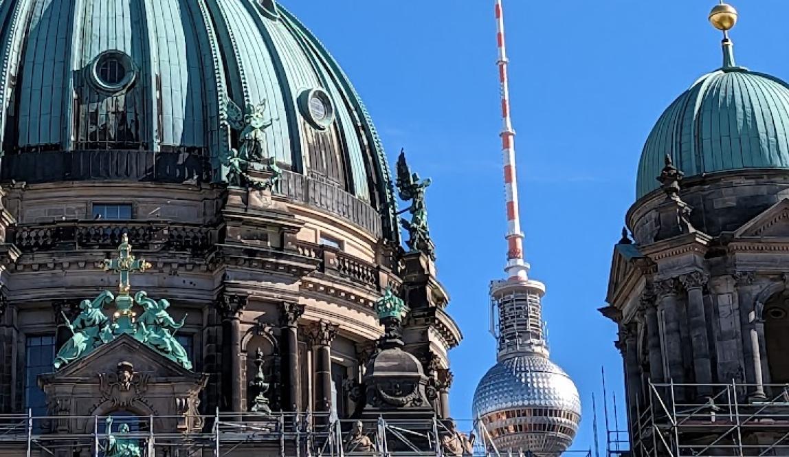 Two copper domes covering bottom left and right of picture, with Berlin Fernsehturm needle in the middle of them in the background