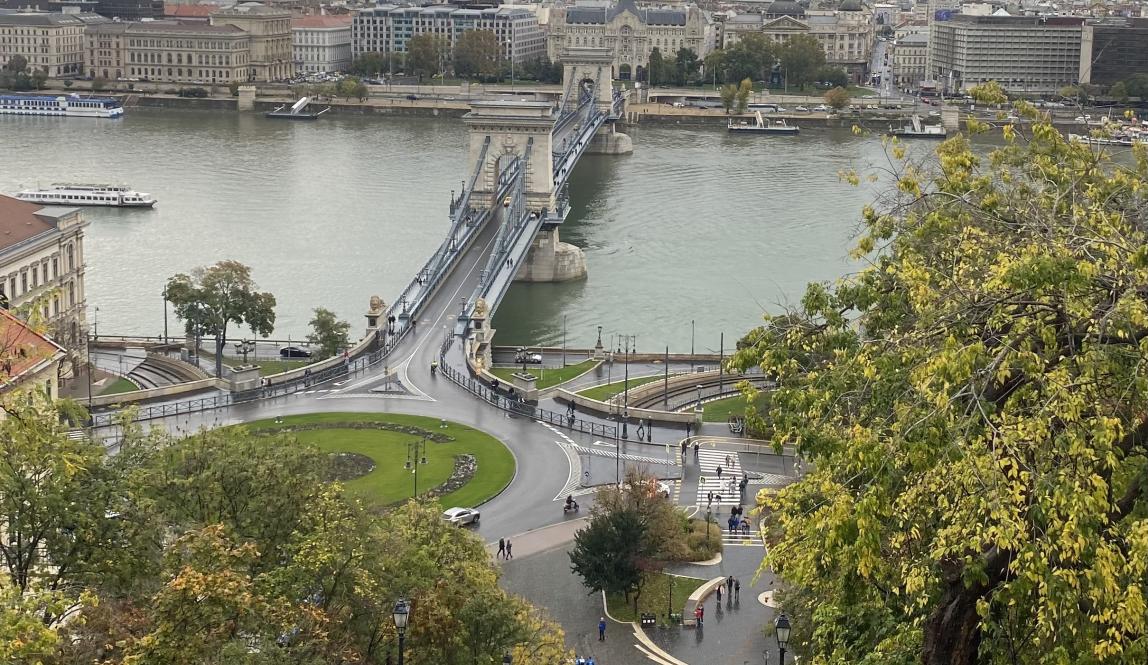 A heightened view of Budapest Parliament, and the roads stretching across a bridge into another district. At the bottom of the photo, it shows the rails of the cable car that brought the photographer to the vantage point.