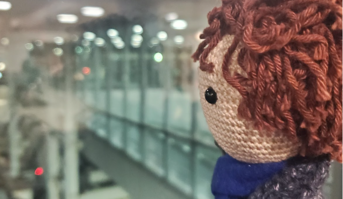 A doll resembling Sherlock from the BBC series "Sherlock staring out the airport window wistfully.