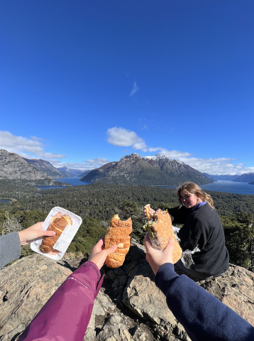 three hands holding a jam and cheese sandwhich on top of a hill