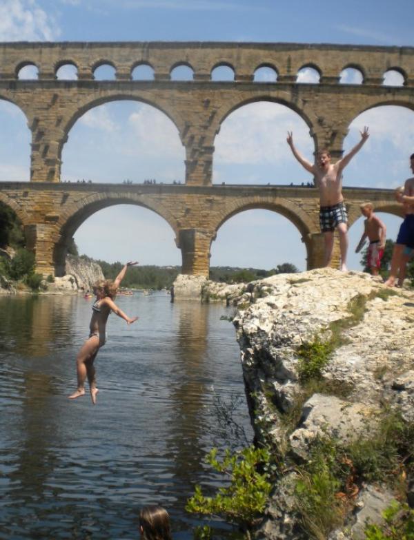 students jumping into a river; one student facing the camera and holding up peace signs.