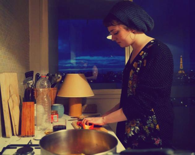 a student in their Paris apartment cooking dinner with the Eiffel Tower visible out the window