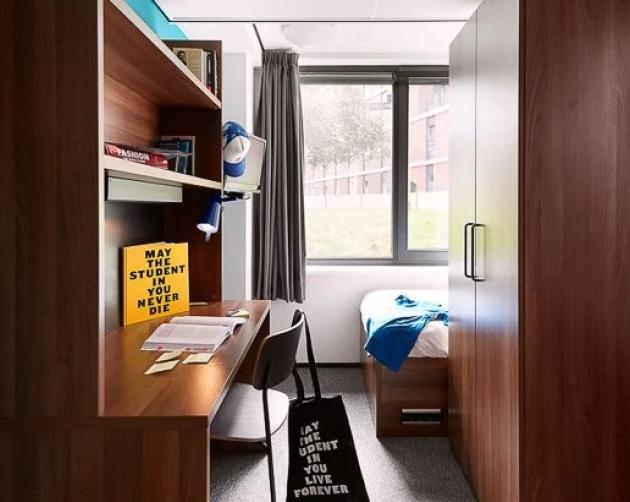 student apartment in amsterdam with wooden furniture including a desk, bed, and tall windows