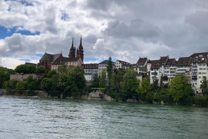 Perspective of the Rhein and Basel Münster, clouds against blue sky, leafy trees, ripples along the river 
