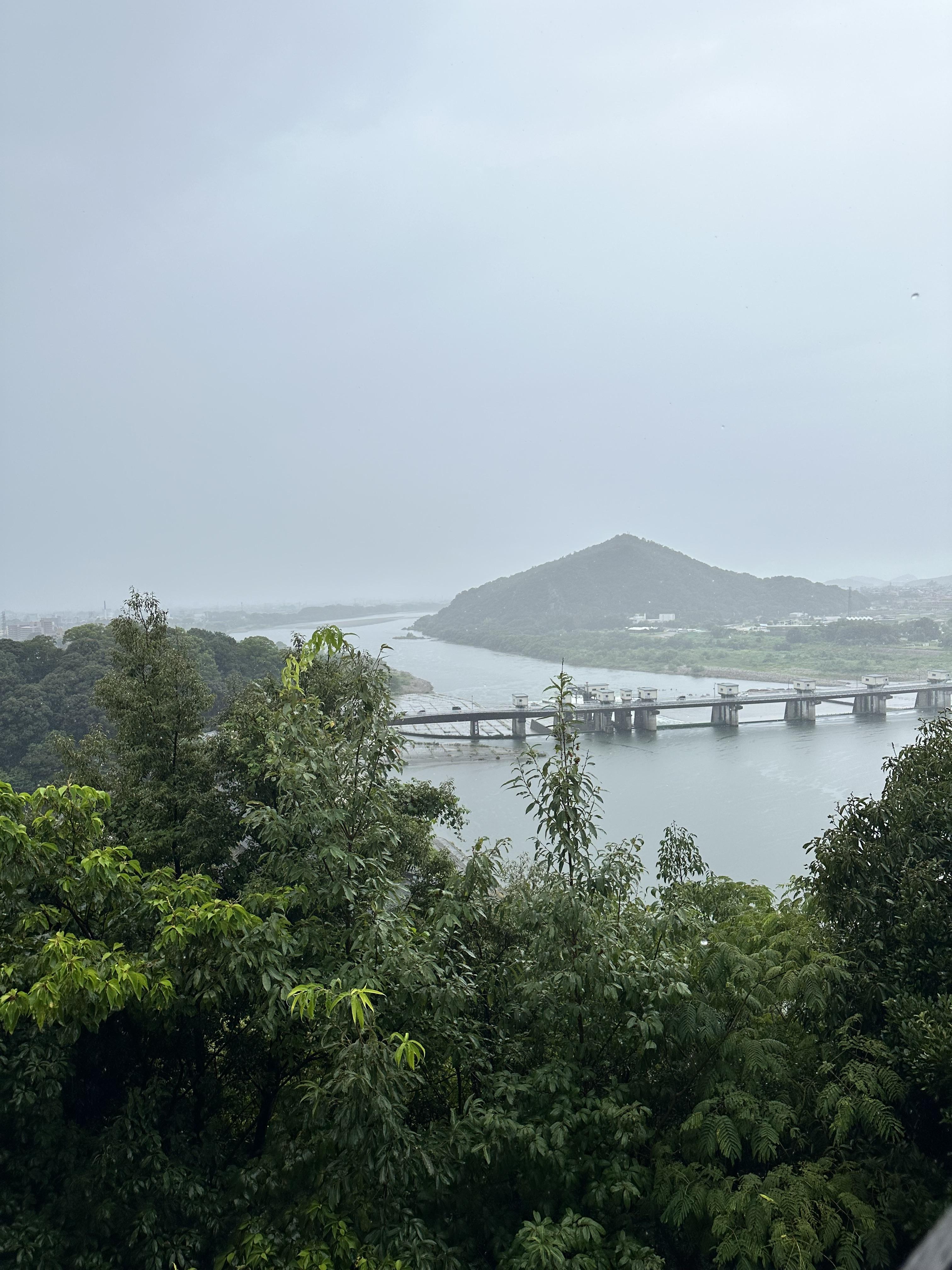 A view from Inuyama castle on a rainy day with a mountain in the back overlooking a river.