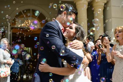 Justin and Monica at their wedding surrounded by guests blowing bubbles