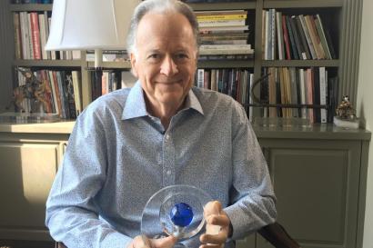 Oscar-Nominated Screenwriter Willard Huyck sitting in front of the bookshelf 