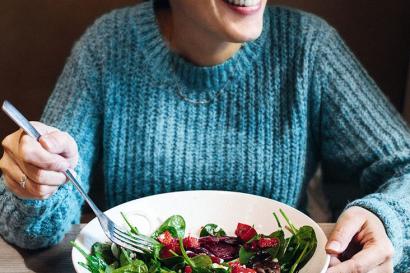 In a booth, a woman in a blue sweater is eating a salad.