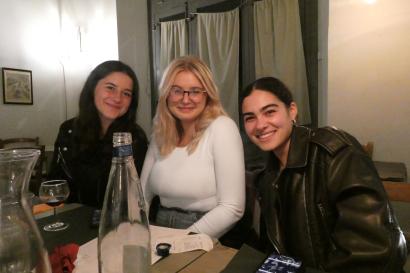 Three girls are sitting together smiling at a table in a dimly lit restaurant in Rome, Italy.