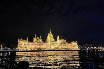The Hungarian Parliament illuminates the Danube river under a night sky.