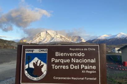 Welcome sign at the check-in point that must be passed to enter the Torres del Paine National Park in the Chilean Patagonia. The sign is framed by a snow-capped mountain that lies in the background.