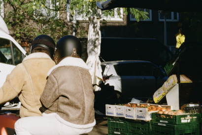 Two people on a moped outside the fruit stand