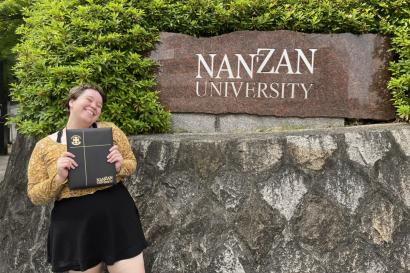 Author, Macks, standing with diploma in front of Nanzan University's sign.