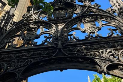 A bronze gothic style gate at the entrance to the Granada Cathedral courtyard, with trees in the background. 