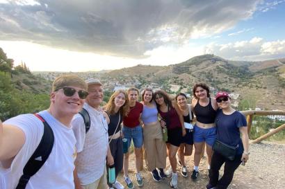 9 students and the program director taking a picture with the view of the the city of Granada in the middle of a hike.
