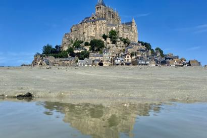 The abbey of Mont Saint-Michel during the day and reflecting in a pool of water.