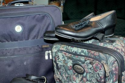 Two packed suitcases, a large one on the left, and a smaller one on the right with a pair of tap shoes sitting on top.