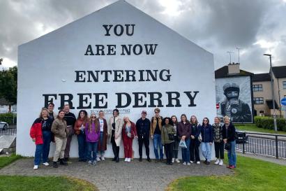 A large group of IES students stand in front of a giant white sign painted on a house, which reads, 'You are now entering Free Derry.'