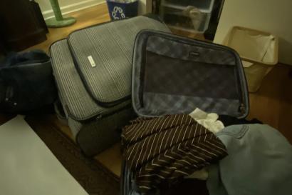 TWO LARGE SUITCASES ON THE FLOOR OF A BEDROOM. ONE IS OPEN AND FULL OF FOLDED CLOTHES.