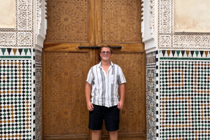 A Moroccan style door with Moroccan tile work, with a handsome blond man standing in the middle. 