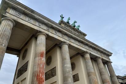 Photo showing overcast sky and the Brandenburg Gate, a neoclassical monument with large arches and a chariot on top.