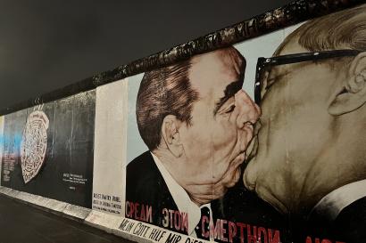Image at night showing a portion of the Berlin Wall with an art display depicting two prominent politicians from the East and West sides of Germany kissing