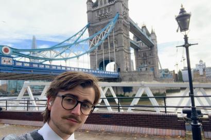 Boy wearing glasses and a sweater poses in front of London's Tower Bridge