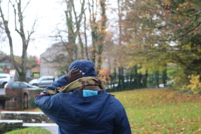 Mariana stands with her back to the camera, a hand on her head. She is dressed warmly in a blue rain jacket, with fall colors in the background.