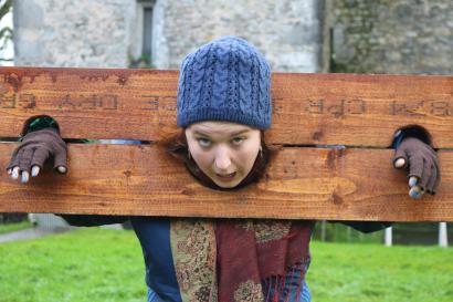 A person is making a silly face in the stocks with Bunratty Castle in the background.