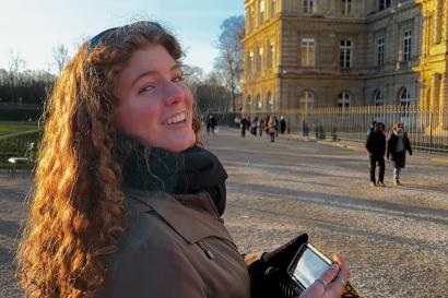 Ginger lady looking back smiling bashfully at the camera with her phone in hand by the Luxembourg gardens.