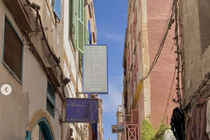 A colorful street with pink, green, and blue walls and shutters on older buildings, ivy hanging over a wall, and signs for a hotel and café.