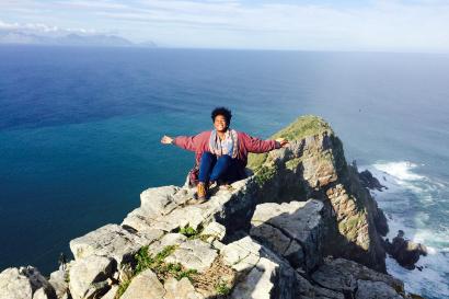 Angela Tetty with arms out sitting on rocks