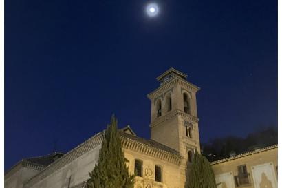 Photo looking up of the tower of a church at night with the moon above the steeple. The sky is very dark blue and there appears to be a ring of light around the moon