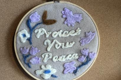 A felt design on an embroidery hoop that says "Protect Your Peace" and is surrounded by flowers