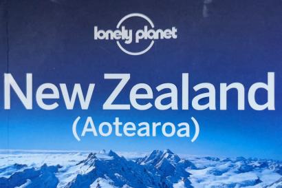 The picture displays the front cover of the book, New Zealand (Aotearoa) by lonely planet. The front cover is dark blue with snowcapped mountains.