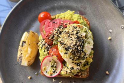 In this photo, there is a slice of cereal toast topped with avocado, tomato, lemon, and a poached egg from The Store in Auckland, NZ.
