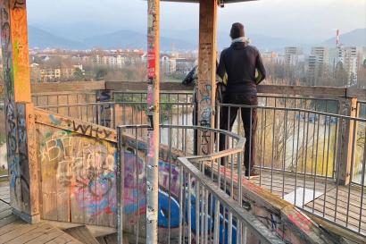 Friends leaning over balcony of wooden tower. Tower covered in graphitti art. Evening light. 