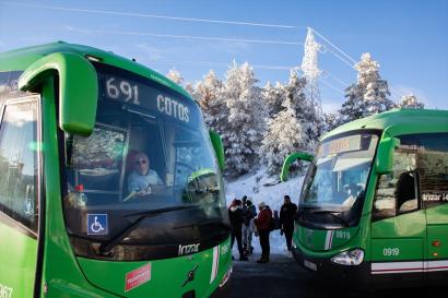Two green public transport busses cross in front of a snowy landscape, far outside of the city of Madrid.